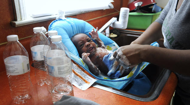 Seorang wanita menggunakan air kemasan untuk mencuci putranya yang berusia tiga minggu di rumah mereka di Flint, Michigan Todd McInturf / The Detroit News / AP